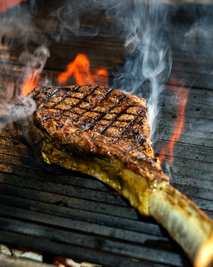 Mouthwatering grilled tomahawk steak sizzling over an open flame, perfect for BBQ enthusiasts.